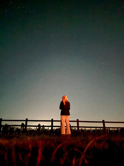 A woman looks over a sunset field while Glamping in Norfolk